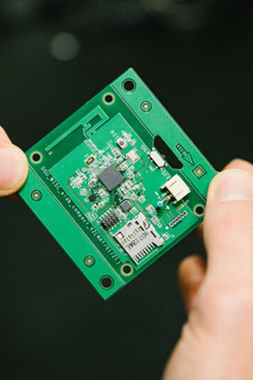 A green microchip is held in between two hands