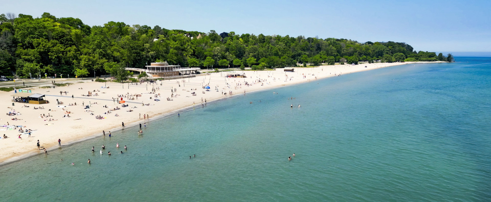 An aerial view of a beach along Wisconsin's coast. People play in the water while others lay on the sandy beach.