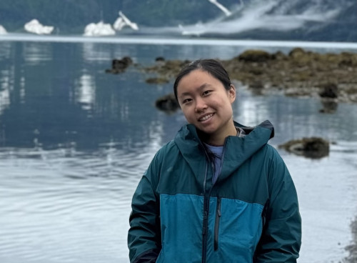 Choi stands in front of a lake and snow covered mountains for portrait photo.
