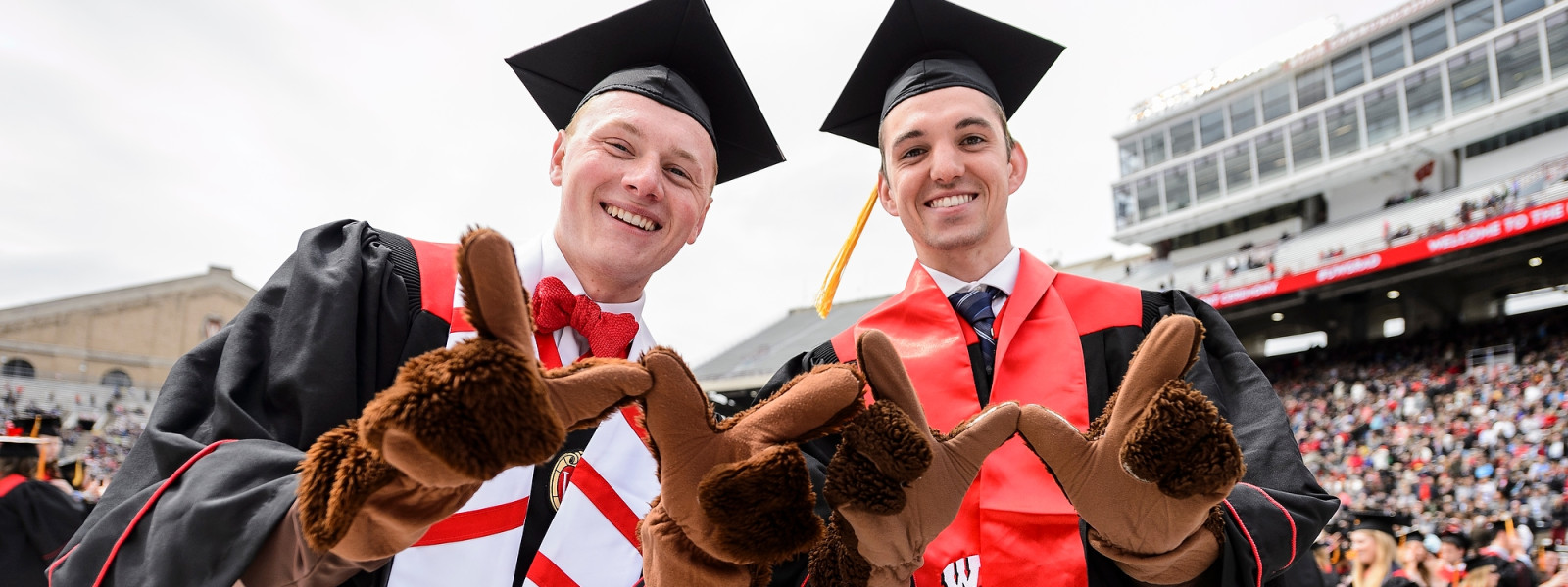 Hoffman and Van Krey each wear fuzzy Bucky Badger mascot gloves and hold their hands in the shape of a 'W' to the camera.