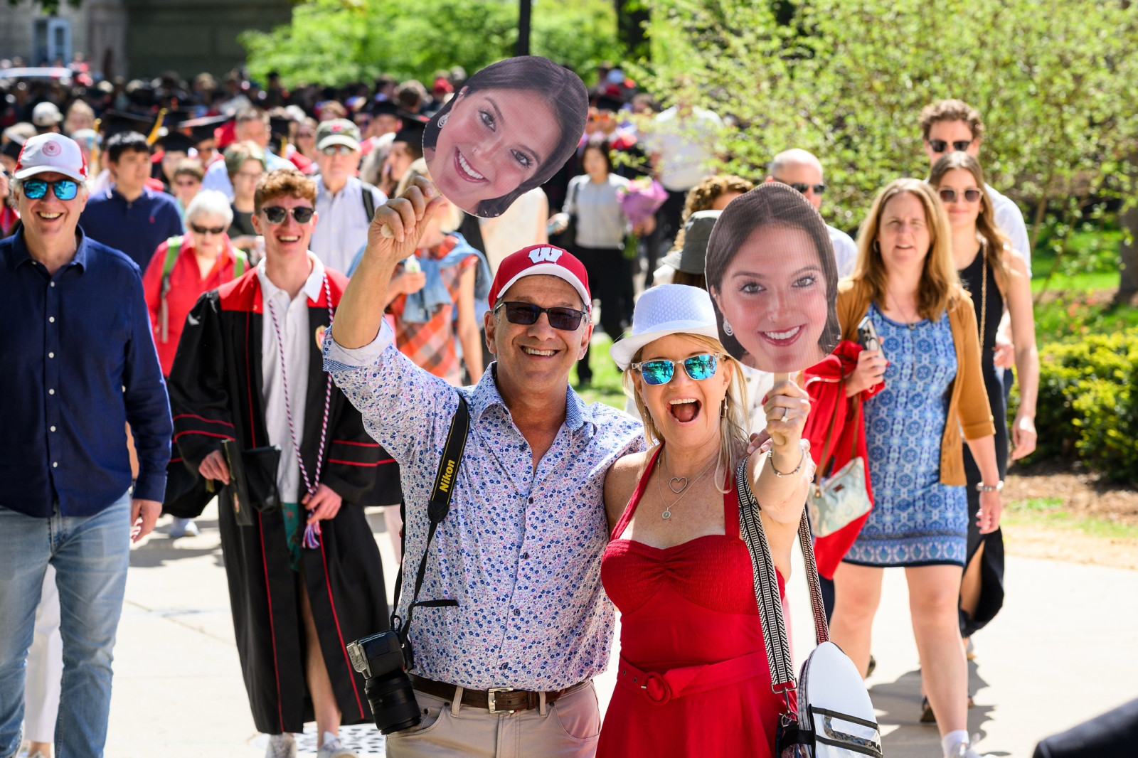 Two people smile excitedly and hold up paper fans with the face of the graduate they've come to support.