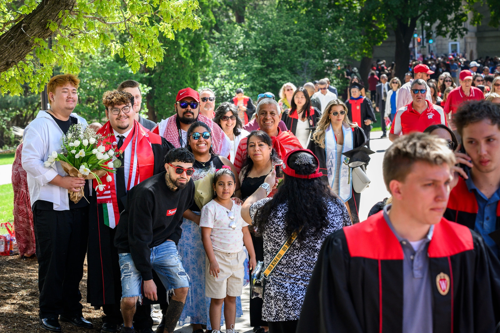Family members gather around a graduate for a group photo outside Camp Randall as a crowd of people walk by.