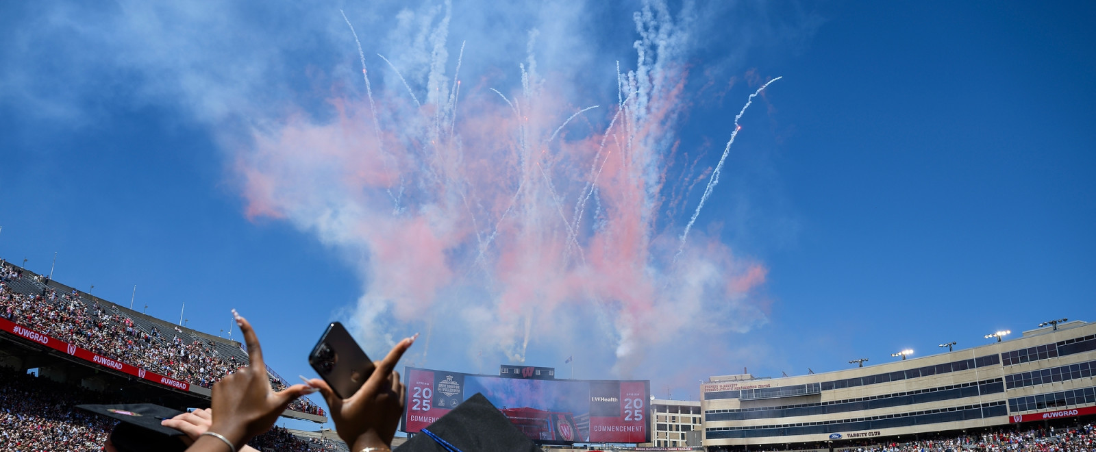 A person raises their hands to make a W as the crowd looks ahead at a fireworks display.