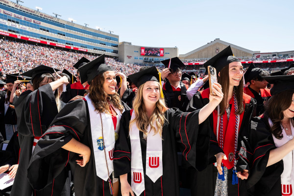Two graduates pose for a selfie photo while celebrating during UW–Madison's spring commencement ceremony at Camp Randall Stadium
