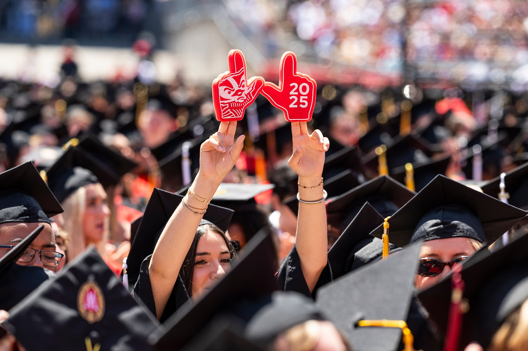 A graduate holds up small foam fingers to make a W.