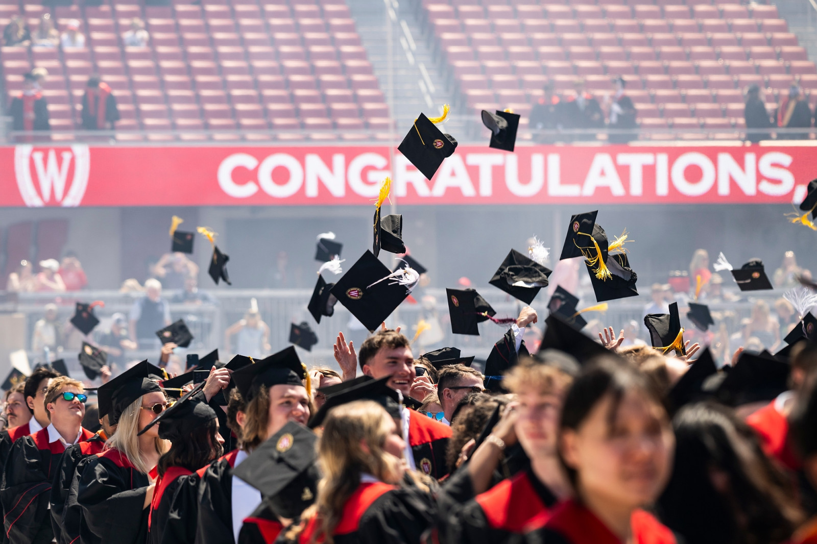A screen in the background reads Congratulations as new graduates toss their caps in the air.