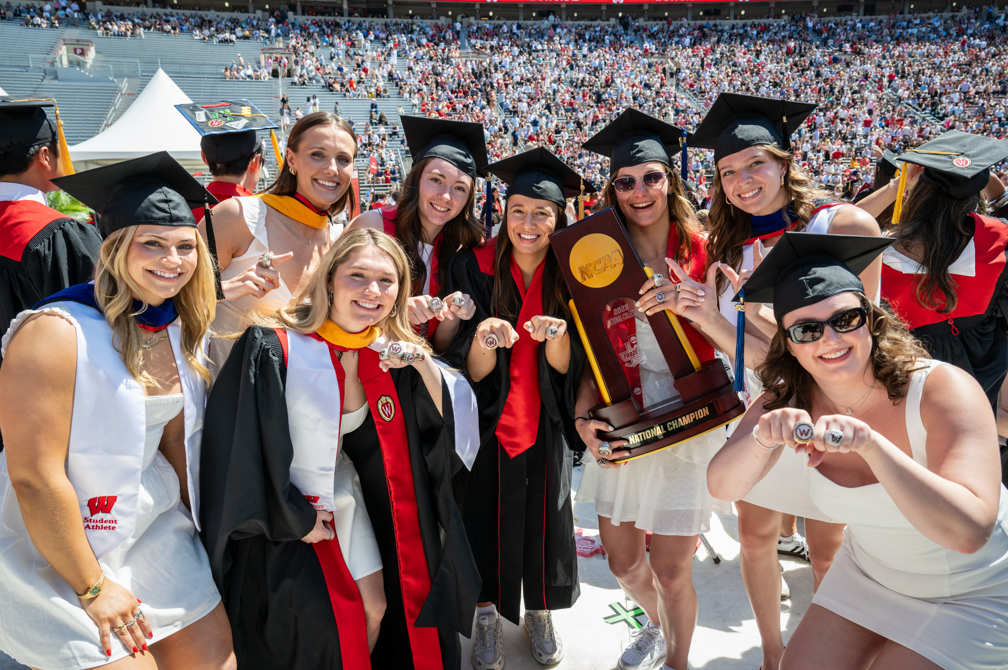 A group of women gather around their championship trophy and show off their championship rings to the camera.