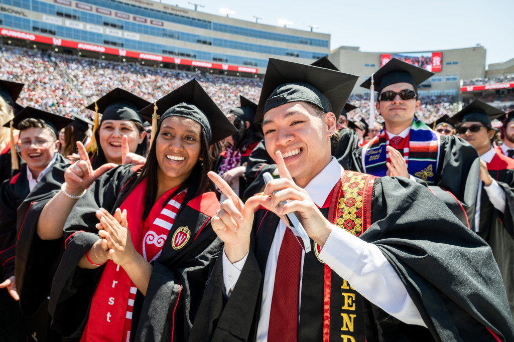 A group of people in graduation gowns and hats smile at the camera.