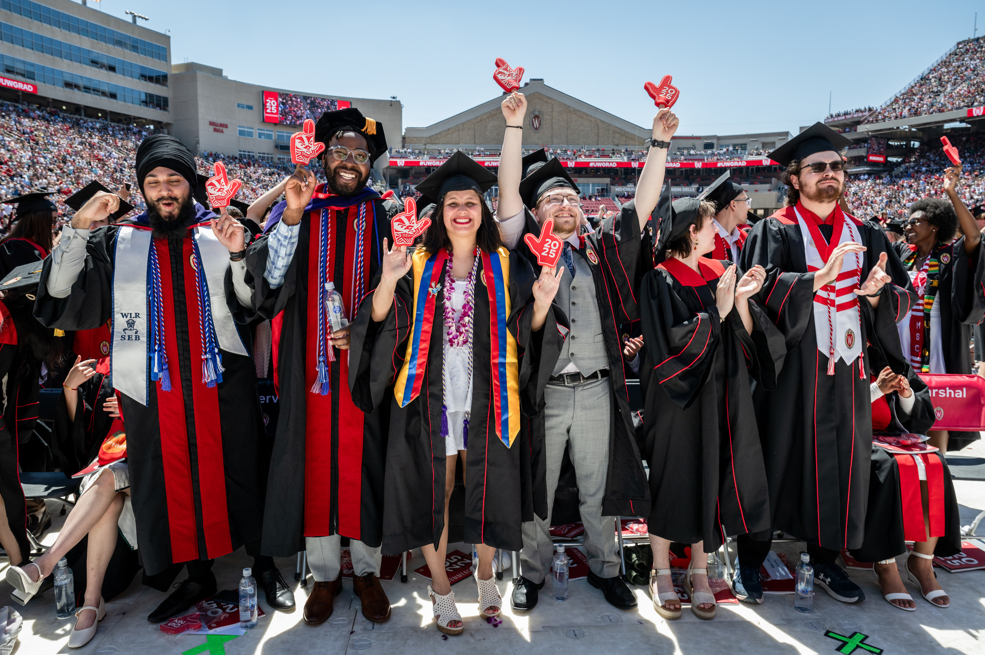 Graduates hold up small foam fingers, one on each hand, to form a Wisconsin W.