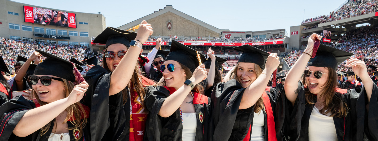Five new graduates standing together move the tassels on their caps from the right side to the left.