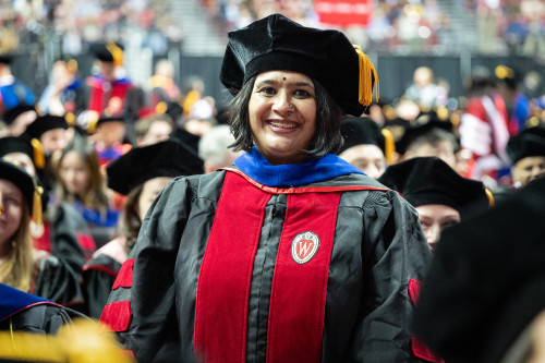 A woman in commencement robes smiles at the camera.