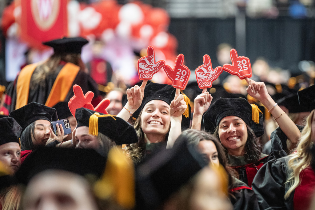 A photo of some smiling, gleeful people in graduation gowns holding up foam fingers.