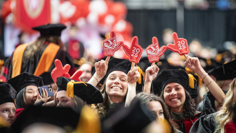 A photo of some smiling, gleeful people in graduation gowns holding up foam fingers.