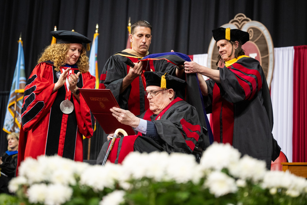 A woman in academic robes gives a diploma to a man.