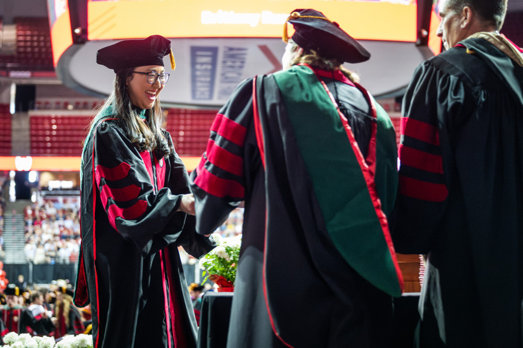A graduate smiles widely as she's given her diploma.