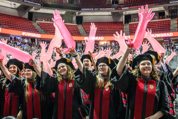 Graduates wave red inflated surgical gloves in the air as they sing the alma mater.
