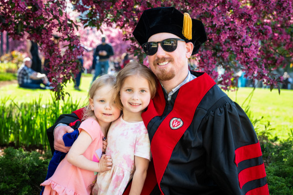 A grad poses for a photo with his two young daughters.