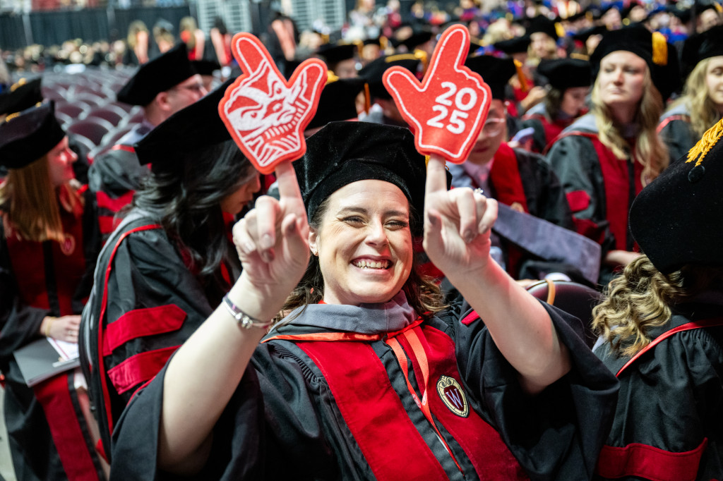 A woman holds up two foam fingers that say Commencement 2025.