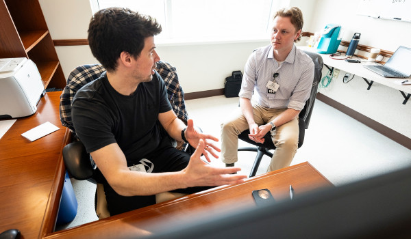 Leiknes sits at a computer and faces Hoffman who sits next to but slightly behind him. Leiknes is explaining patient details to Hoffman prior to entering treatment room.