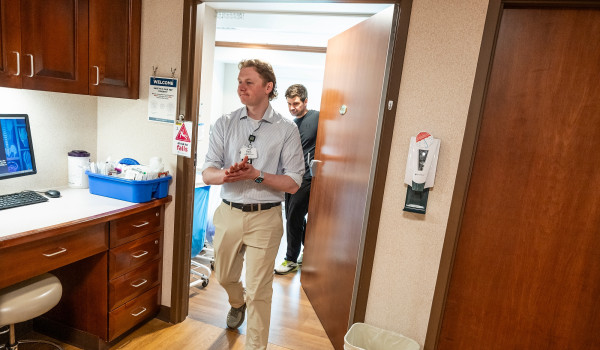 Hoffman walks into a treatment room at Aurora Medical Center–Manitowoc County followed closely by Leiknes whose hand remains on the door of the treatment room as he pulls it shut. As they enter, they are greeted by dimmer lights and a computer that partially shows x-rays of an unidentified patient.