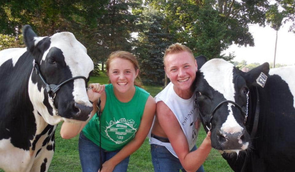 Hoffman and his sister stand side by side. Each are flanked by a black and white beef cow with harnesses, which Hoffman and his sister hold in their hands as they smile for the photo.