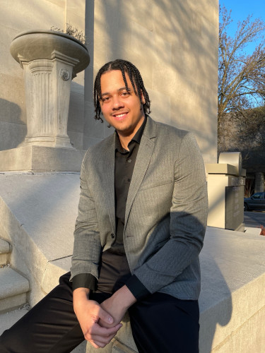 Jadius McGhee smiles for a portrait photo on the steps of a stone building.