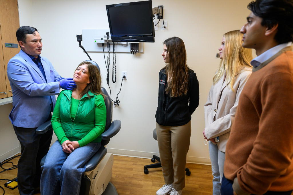 A doctor feels a seated patient's neck as two other people observe.
