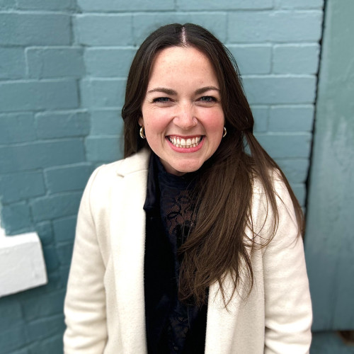 Liz Olson smiles for a photo taken against a blue brick wall