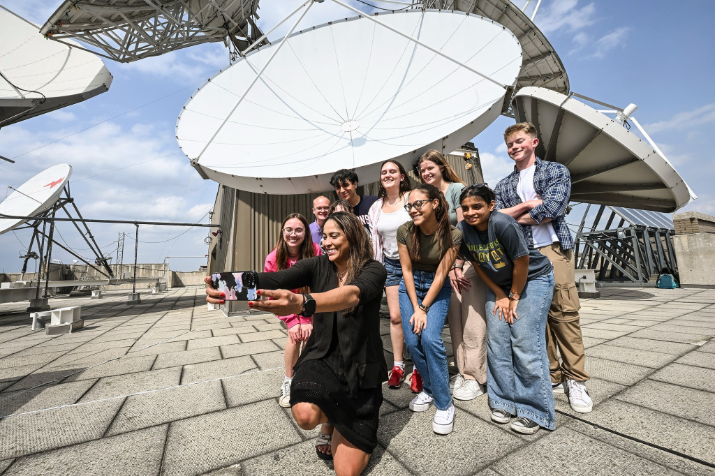 A group of people work together around a satellite dish on the top of a tall building.