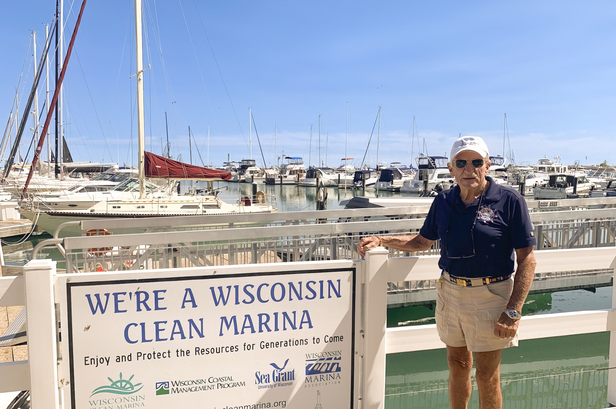 A man rests his hand on a clean marina sign that is posted along a fence at the edge of a Wisconsin marina.