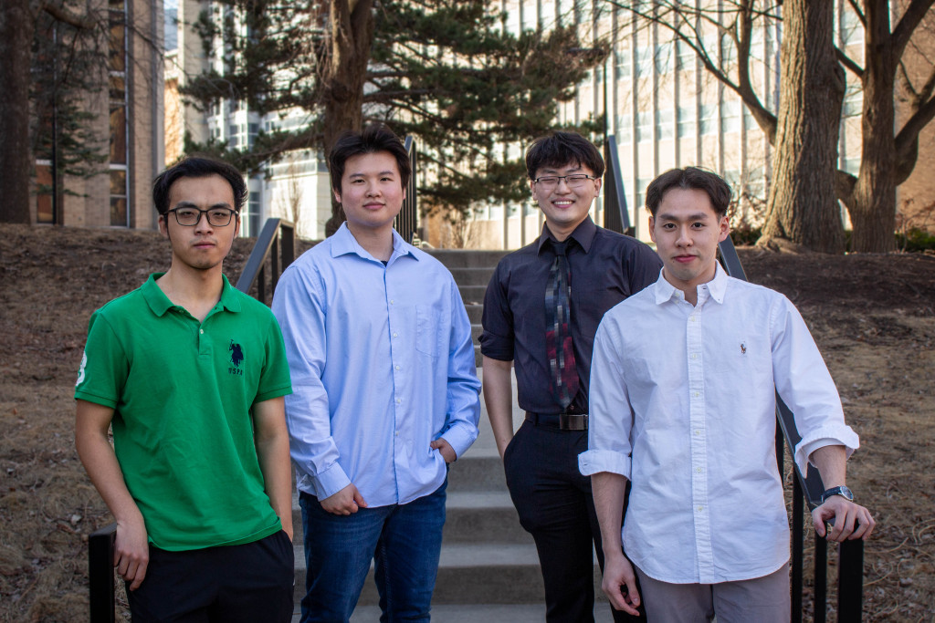 Zhou, He, Zhu and Chen pose on cement stairs outside of a campus building.