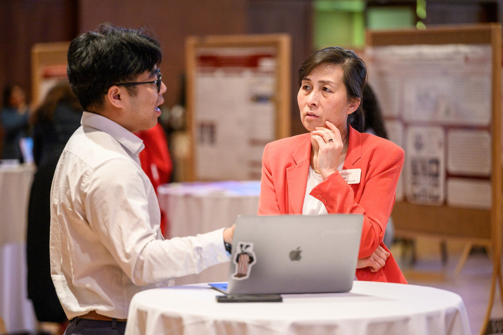 Two people talk as they look a laptop computer on a table.
