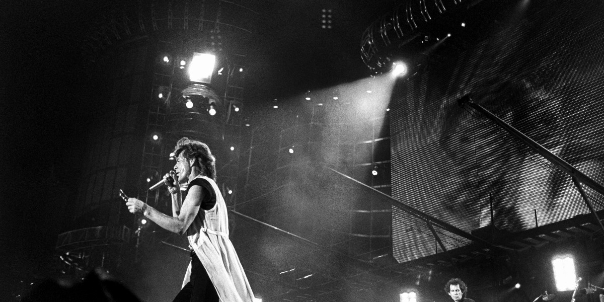 A close-up of Rolling Stones lead singer Mick Jagger on the mic and Keith Richards on guitar on stage, with a large video screen and scaffolding in the background.