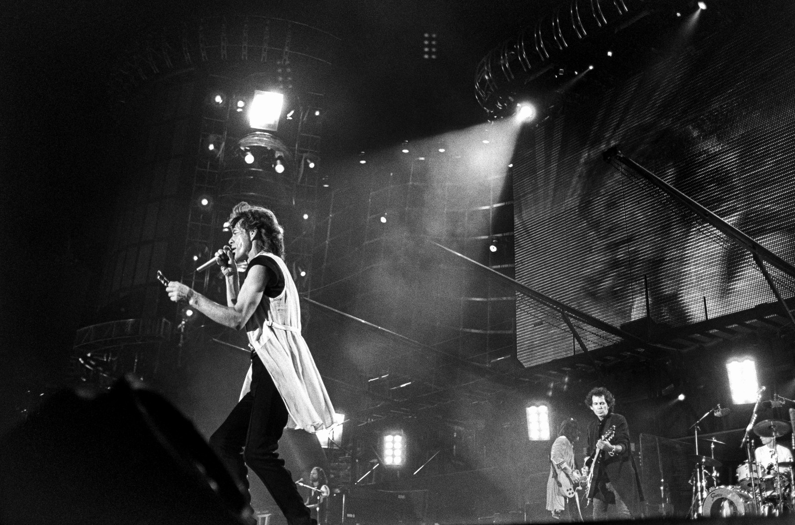 A close-up of Rolling Stones lead singer Mick Jagger on the mic and Keith Richards on guitar on stage, with a large video screen and scaffolding in the background.
