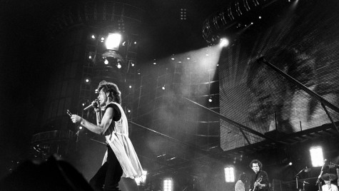 A close-up of Rolling Stones lead singer Mick Jagger on the mic and Keith Richards on guitar on stage, with a large video screen and scaffolding in the background.