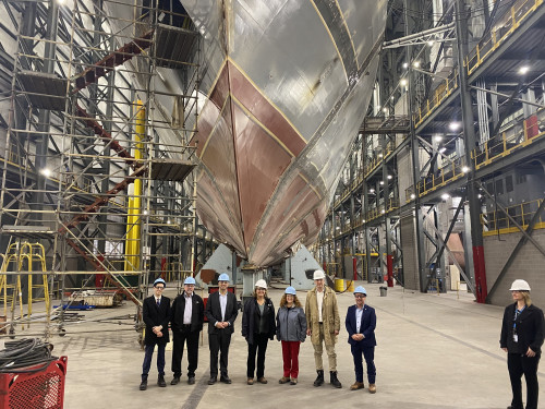 A group of people stand in a huge shipyard with a big boat in the background.