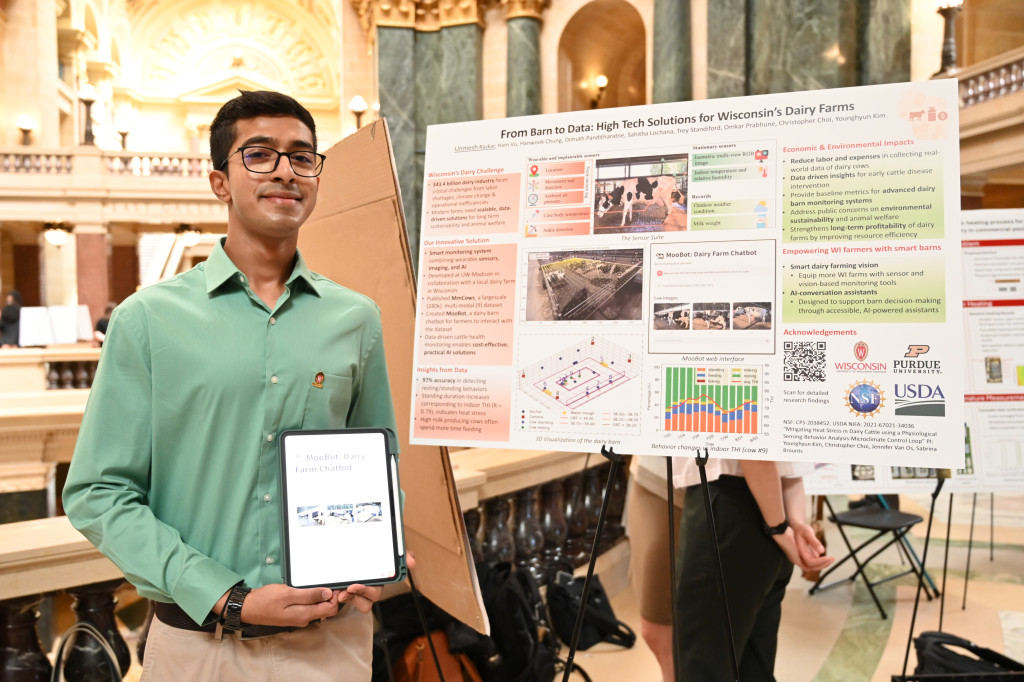 Raskar stands next to a tripod stand that holds his research poster. In his hands, he holds an iPad that displays the tool he had developed as part of his research.