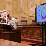 Hoefferle stands behind a heavy wooden podium in a marble-walled room of the State Capitol Building. She directs herself and points to a nearby TV screen that displays her research.