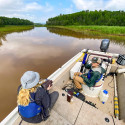 A person sits in an open motor boat on a water way.