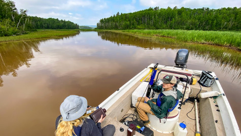 A person sits in an open motor boat on a water way.
