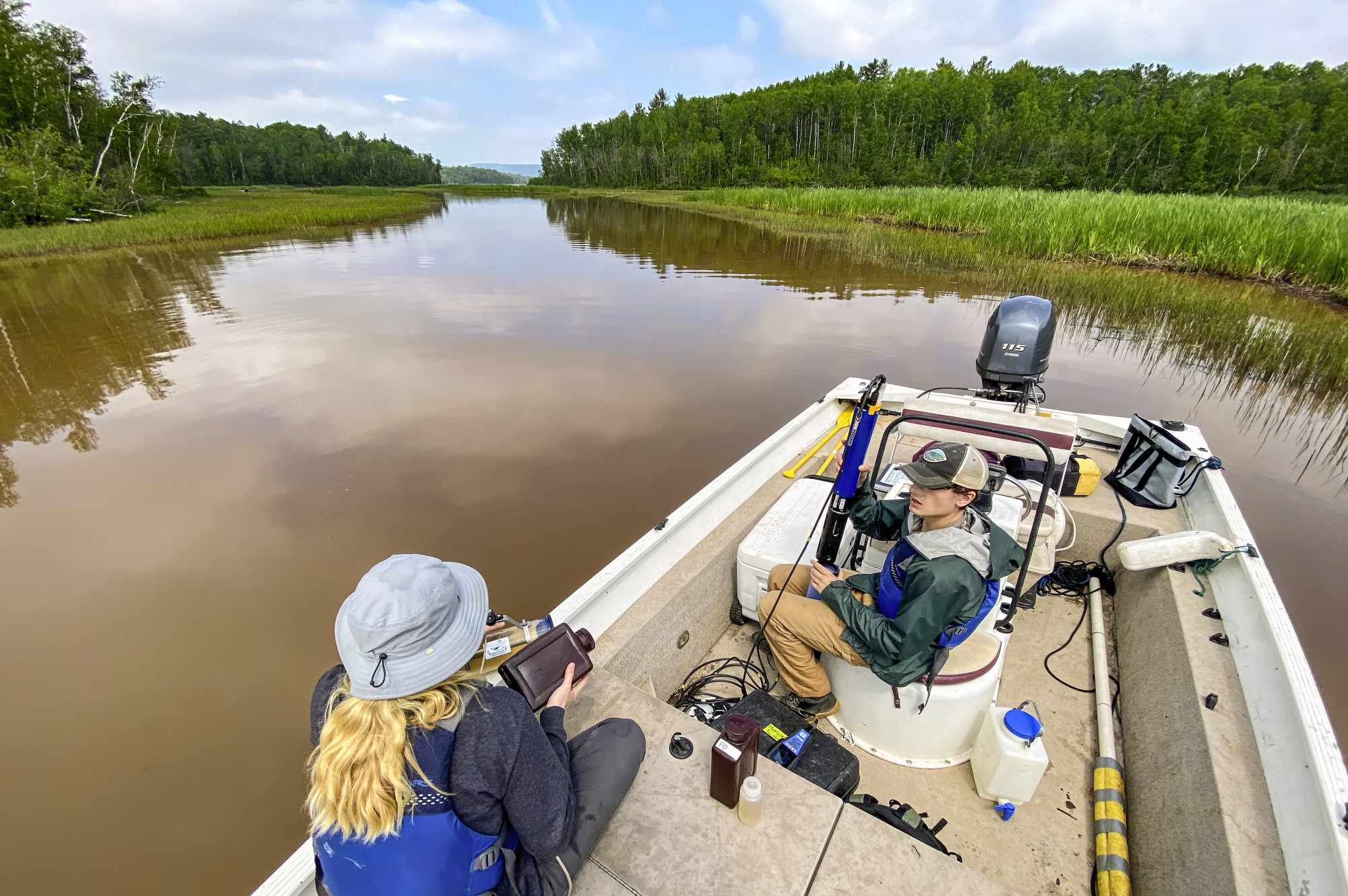 Two researchers sit in a speedboat on one of Wisconsin's many waterways. The boat is stopped as on researcher unravels cord and the other prepares a large vial to gather samples.