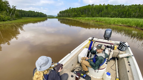 Two researchers sit in a speedboat on one of Wisconsin's many waterways. The boat is stopped as on researcher unravels cord and the other prepares a large vial to gather samples.