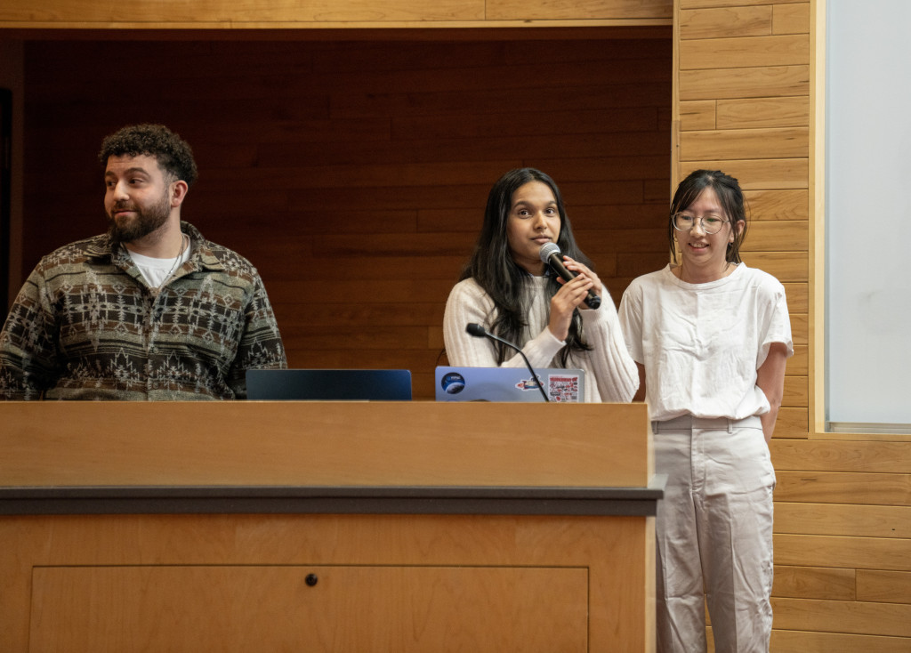 A young woman holds the microphone and addresses the class from behind the podim.