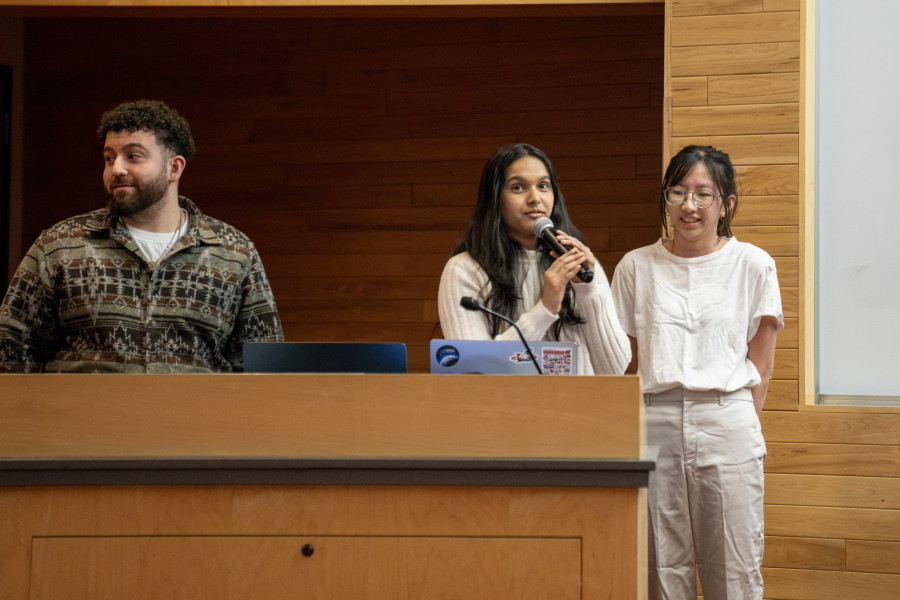 A young woman holds the microphone and addresses the class from behind the podim.