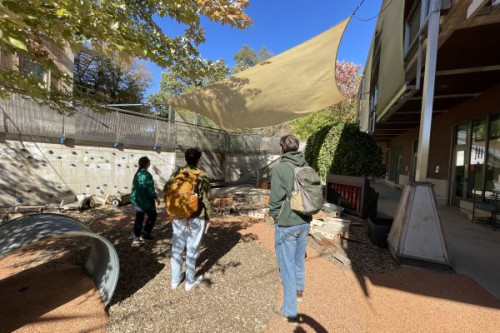 Several students look at a canvas sail stretched over an outdoor classroom.