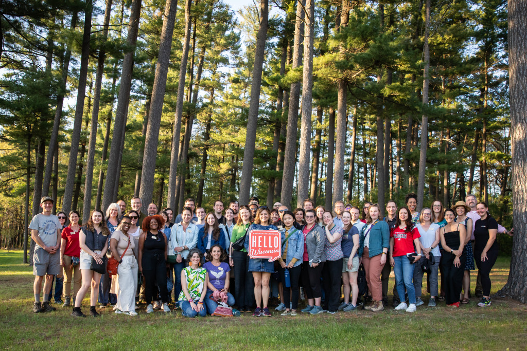 A group of people standing in the woods amid tall trees pose for a photo.