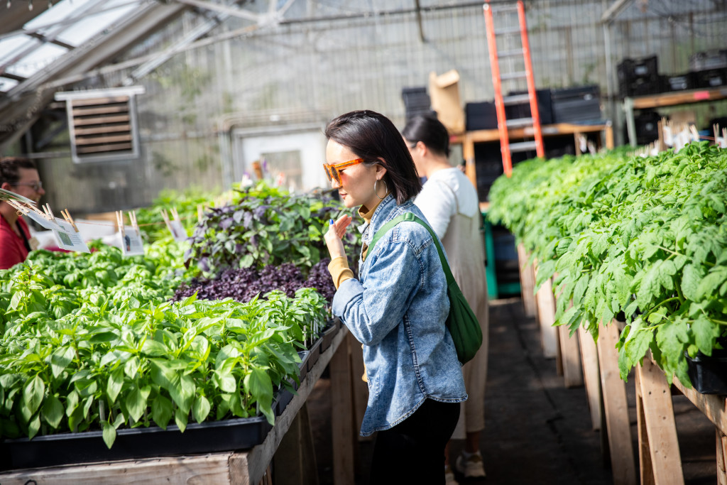 A woman stands amid green plants, smelling their scent.