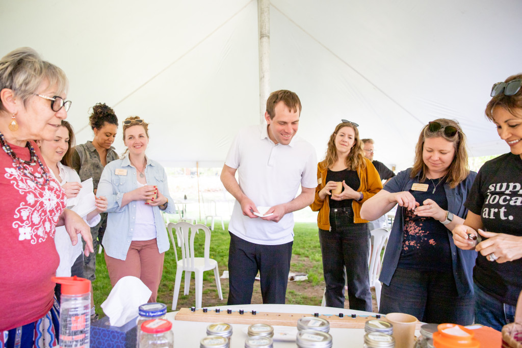 People surround a table holding various plants and herbs, and they look at them and hold them.