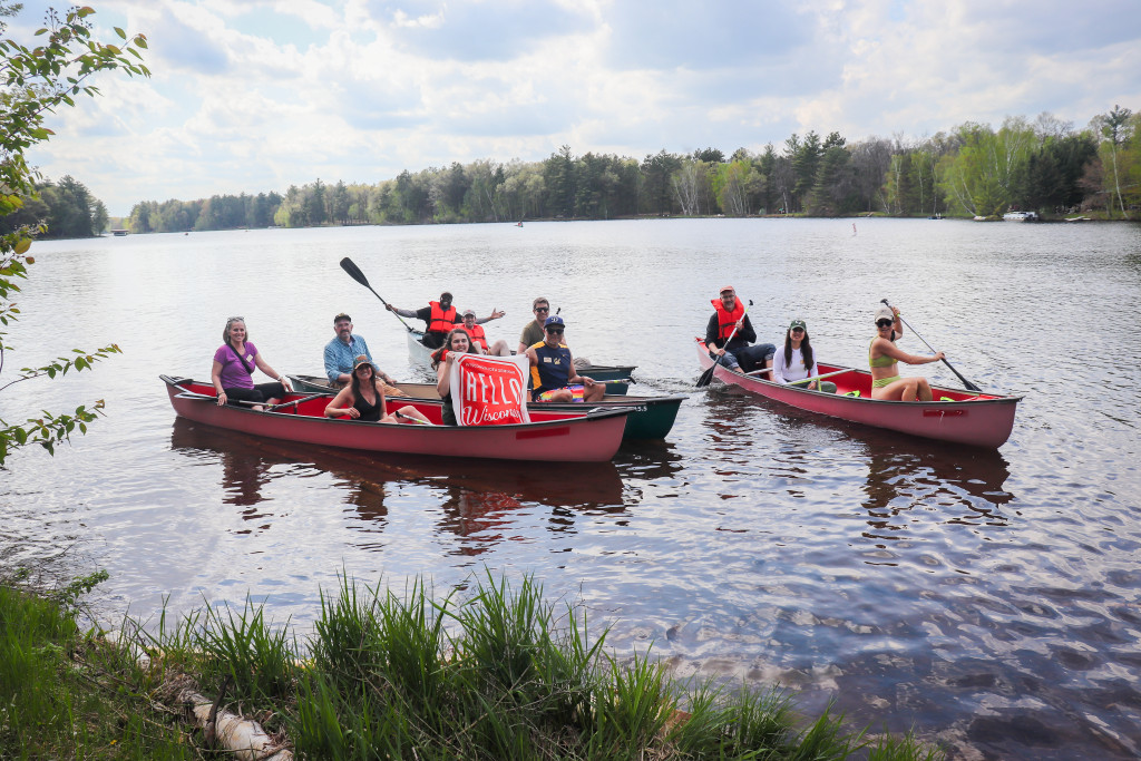 People in two canoes on a lake wave to the camera and smile.