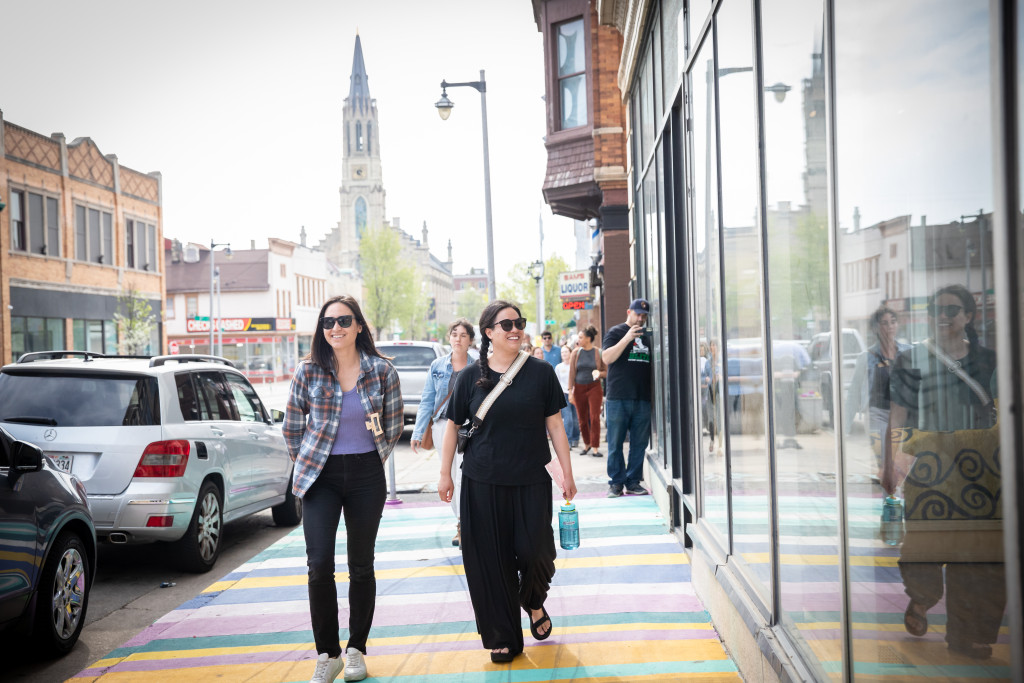 Two women walk along a sidewalk in a downtown area.